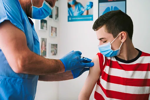 Doctor giving teenager boy vaccine.